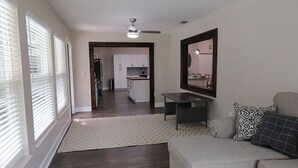 A spacious living room with a dark wood floor, a gray sofa, a ceiling fan, and a kitchen in the background. - Sandy Toes Paradise (Palm Coast)