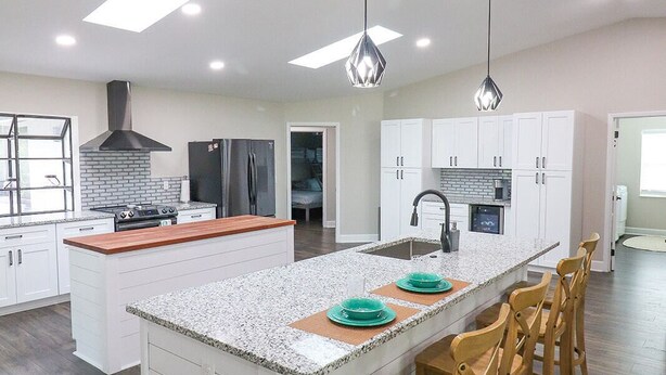 A modern kitchen with a central island, white cabinetry, and a wood floor. - Sandy Toes Paradise (Palm Coast)