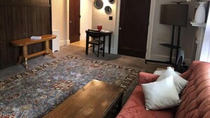 A living room with a patterned rug, a wooden coffee table, a red sofa, a small table with a red bowl, and a TV stand with a TV and a vase with flowers. - 🤓Clever Studio🍷Free Wine☕️Coffee / Tea Bar - Free Parking! (Dover)