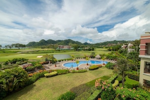 A resort with a pool, lush greenery, and a golf course in the background. - Del Mar 3C 3 bdr Ocean View in Los Suenos (Playa Herradura)