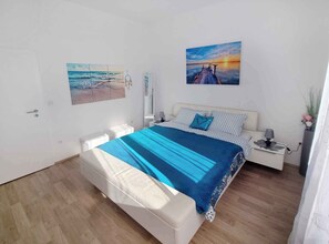 Quarto com cama, mesas de cabeceira, espelho e duas pinturas na parede.