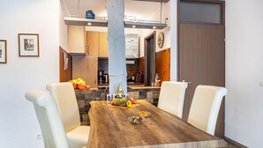 Un coin repas avec une table en bois, des chaises blanches et une cuisine en arrière-plan.