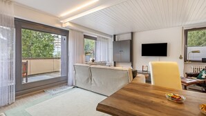 Un salon moderne avec une table à manger en bois, un canapé, un téléviseur et une vue sur l’extérieur.