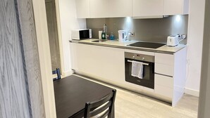 Eine moderne Küche mit weißen Schränken, einem Backofen von Bosch, einer Mikrowelle, einer Spüle und einem schwarzen Esstisch mit Stühlen.