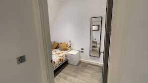Ein Schlafzimmer mit einem Bett, einem Nachttisch, einem Spiegel und einem Lichtschalter an der Wand.