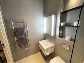 A modern bathroom with a towel rack, sink, mirror, and shelves with toiletries.