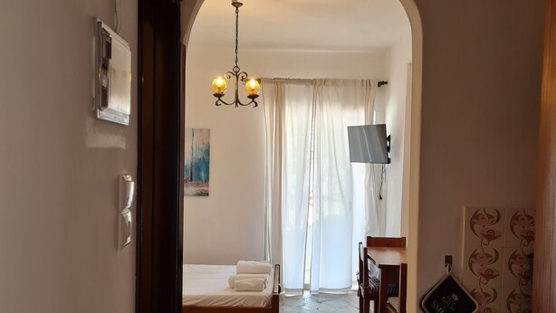 Camera da letto con pavimento in pietra, un letto, un lampadario, una televisione e un bagno visibile attraverso un arco.