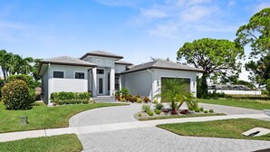 A two-story residential house with a driveway leading to the entrance, surrounded by well-maintained lawns and a variety of shrubs and small trees. - Luxurious retreat on Marco Island  (Marco Island)