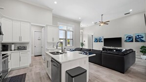 A modern kitchen with white cabinetry, a central island, and a black leather sofa in the living area. - Luxurious retreat on Marco Island  (Marco Island)
