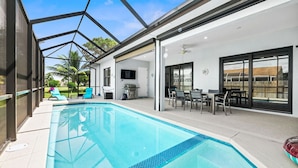 A modern indoor swimming pool with a glass ceiling, surrounded by a patio area with outdoor seating and a view of palm trees. - Luxurious retreat on Marco Island  (Marco Island)
