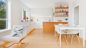 A modern kitchen with white cabinets, a wooden dining table, and a comfortable chair with a floral cushion.