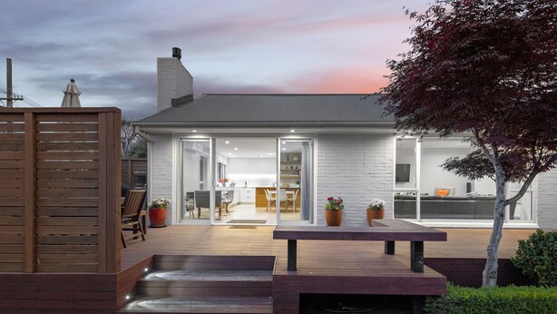 A modern house with a patio, outdoor seating, and a visible kitchen area.