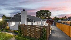 A modern house with a well-maintained garden, a wooden fence, and a clear sky.