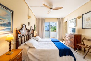 A hotel room with a bed, a ceiling fan, a dresser, a TV, and a balcony with curtains.