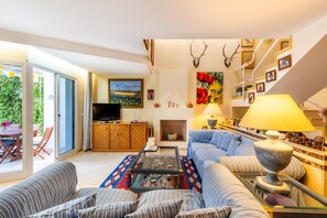 A living room with a sofa, coffee table, fireplace, television, and a staircase with framed pictures. - Chalet 'Dominion Beach' with Mountain View, Shared Pools, Terrace, A/C & Wi-Fi (Estepona)
