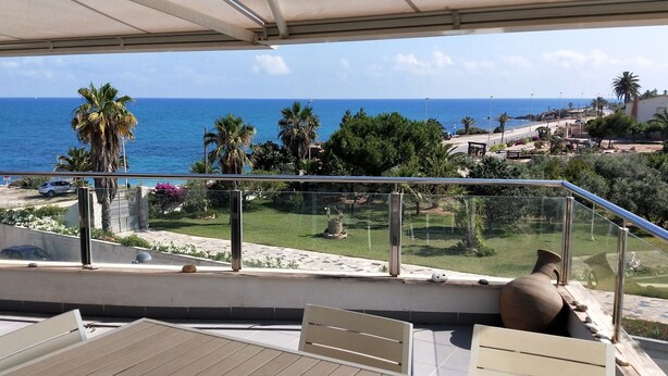 Un balcone con vista sul mare, palme e un giardino.