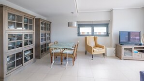 Un soggiorno moderno con un tavolo da pranzo in vetro, sedie in vimini, una poltrona in pelle, una televisione e un mobile contenitore a incasso con ante in vetro.