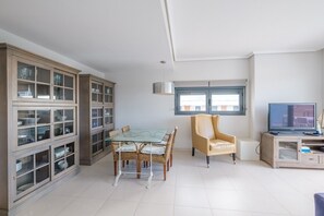 Una sala de estar moderna con una mesa de comedor de vidrio, sillas de mimbre, un sillón de cuero, un televisor y un armario empotrado con puertas de cristal.