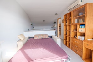 A bedroom with a bed, bedside tables, a wardrobe, and a kitchenette area.