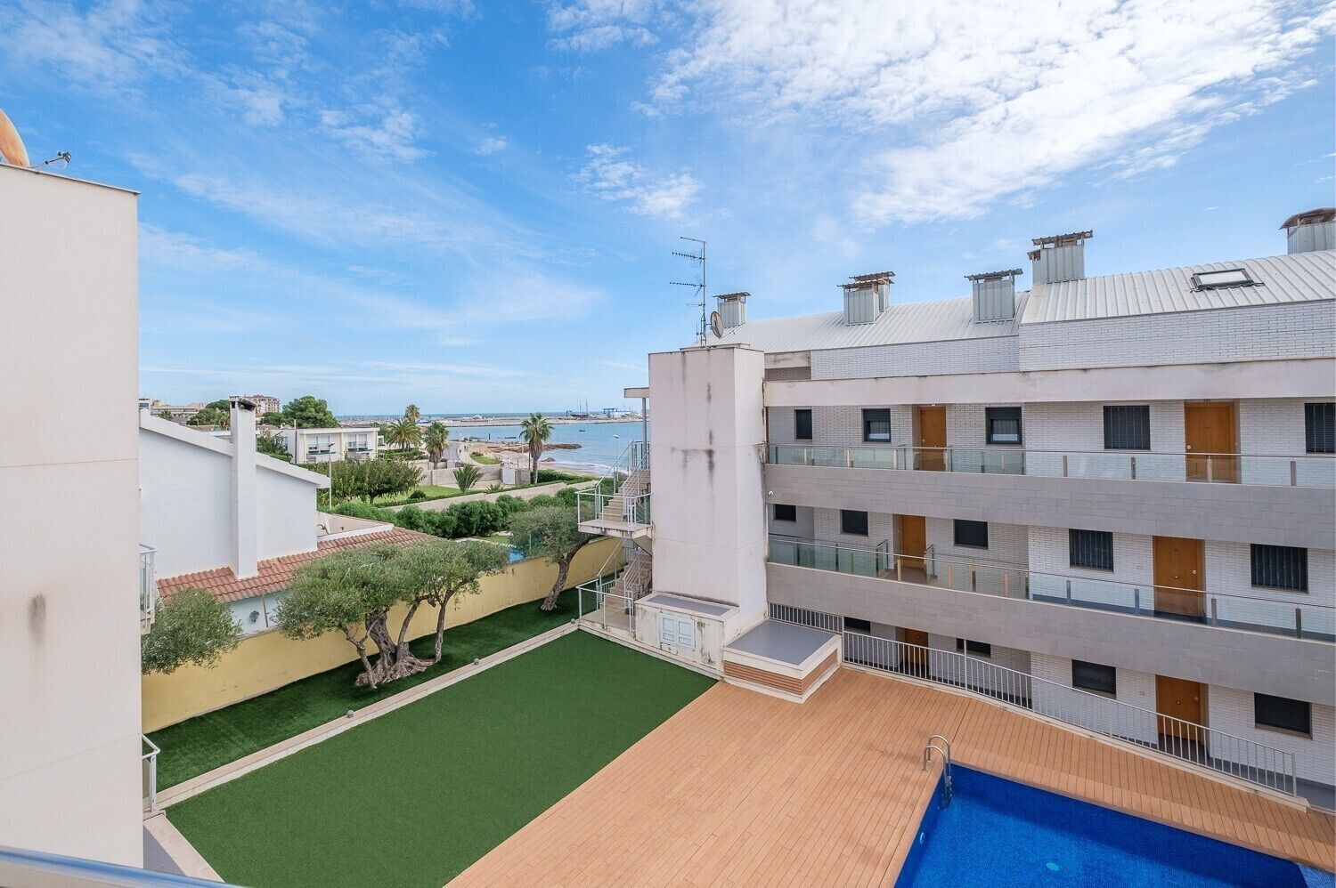 A multi-story building with a rooftop pool, a view of the sea, and a landscaped garden.