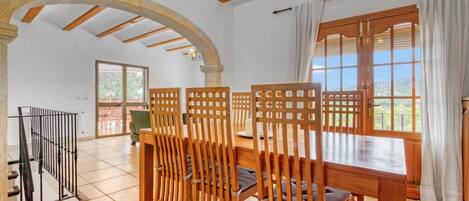 Un área de comedor con sillas de madera y una mesa, una escalera y vistas por una ventana.