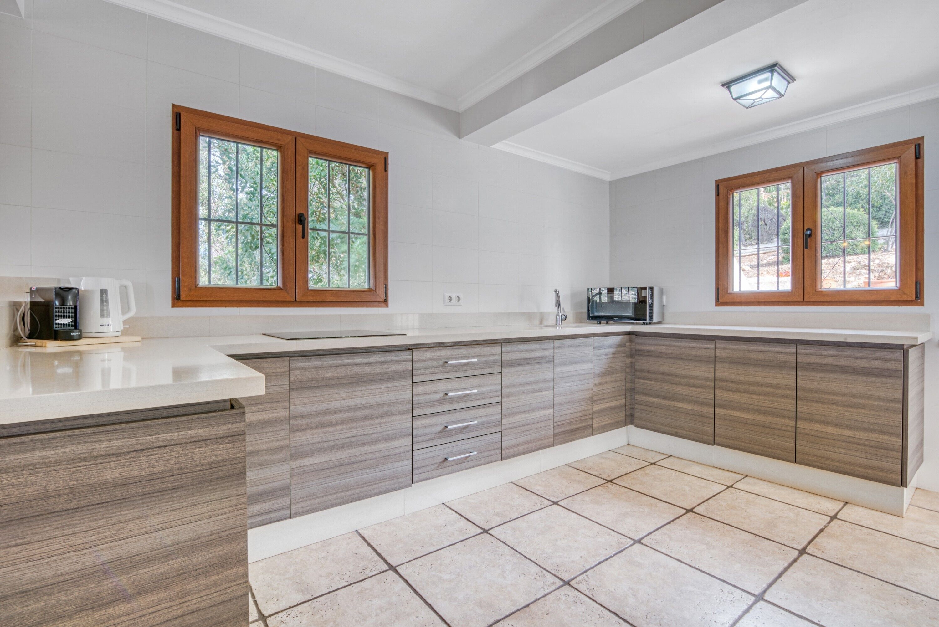 A modern kitchen with wooden cabinets, a countertop, and two windows with wooden frames.