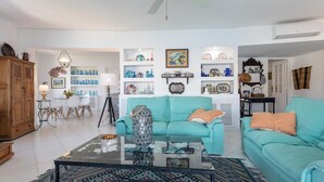 A living room with a teal sofa, a glass coffee table, and a patterned rug. There are shelves with decorative items and a wooden cabinet. - Villa "Casa San Cayetano" with Sea View, Pool, Garden, Terrace and Balcony (La Herradura)