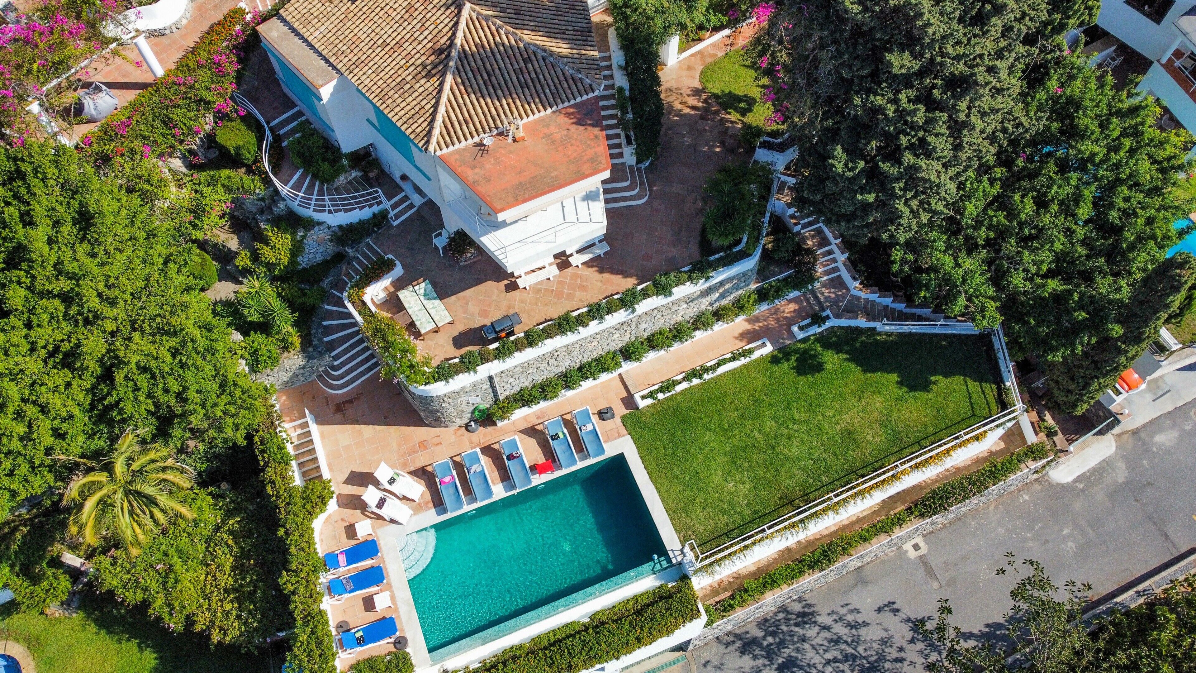 An aerial view of a resort with a swimming pool, lounge chairs, and a large building with a tiled roof.