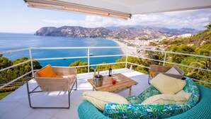 A balcony with wicker furniture, a wooden table, and a view of the ocean and mountains. - Villa "Casa San Cayetano" with Sea View, Pool, Garden, Terrace and Balcony (La Herradura)