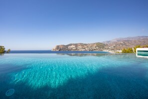 Una piscina infinita con agua azul cristalina, vista al mar y montañas lejanas.