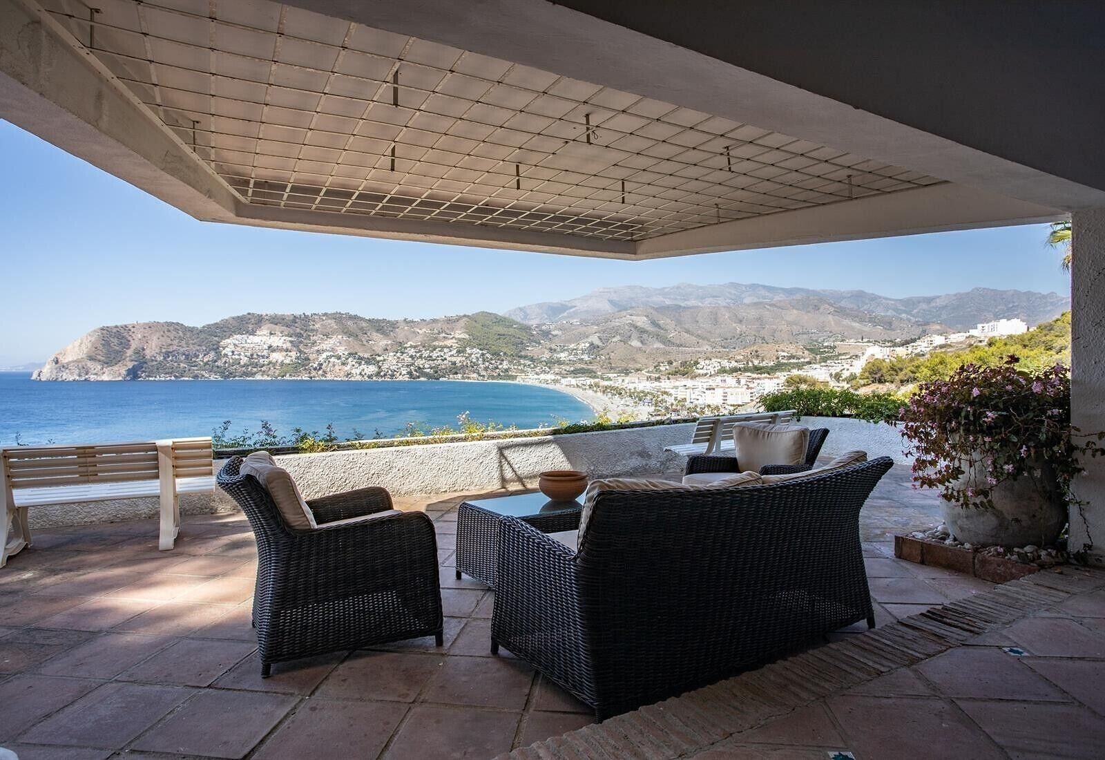 An outdoor patio with wicker furniture, a table, and a bench.