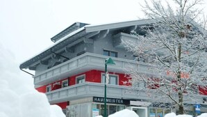 A multi-story building with a red and white facade, a visible sign reading "HAUS MEISTER," and a snow-covered tree in the foreground. - Apartment Siegl by Interhome (Zell am See)
