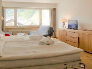 Een hotelkamer met twee bedden, een bureau, een televisie en uitzicht op een bergachtig landschap.