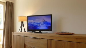 A wooden cabinet with a flat-screen TV on top, a lamp, and a plate. - Beaulieu by Interhome (Zermatt)