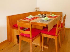 Een eethoek met een houten tafel, stoelen, rode kussens en een rood tafelkleed.