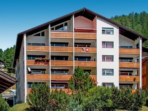 Een hotel met meerdere verdiepingen en balkons, met op de achtergrond een skigebied en een heldere lucht.