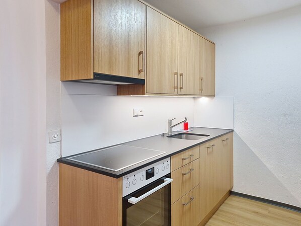 A modern kitchen with wooden cabinets, a stainless steel countertop, a built-in oven, and a sink.