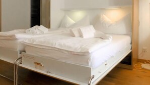 A modern hotel room with a neatly made bed, a bedside table, and a wall-mounted lamp. - Beaulieu by Interhome (Zermatt)