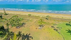 A beach view with a clear sky, ocean, and sparse vegetation. - One bedroom beachfront apartment (Yeppoon)