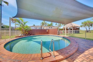 A swimming pool with a brick border, a shaded area overhead, and a fenced yard with palm trees. - One bedroom beachfront apartment (Yeppoon)