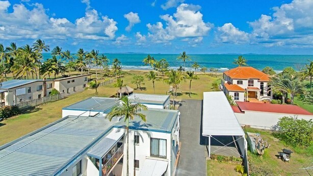A coastal area with multiple buildings, including a prominent house with a red roof and a smaller structure with a blue roof. - One bedroom beachfront apartment (Yeppoon)