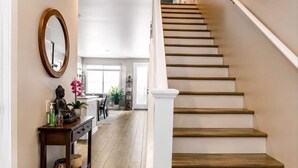 Un escalier avec des marches en bois et des rampes blanches, menant à une pièce dotée d’une grande fenêtre et d’un plancher en bois.