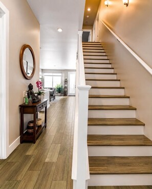 Eine Treppe mit Holzbalken und weißen Geländern, die zu einem Raum mit einem großen Fenster und Holzboden führt.
