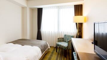 A hotel room with a bed, a desk with a television, a chair, and a window with curtains.