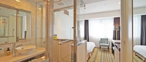 A hotel room with a glass-enclosed shower, a bed, a desk, and a chair.