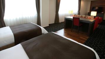 Quarto de hotel com duas camas, uma escrivaninha, uma cadeira, uma televisão e um tapete estampado.