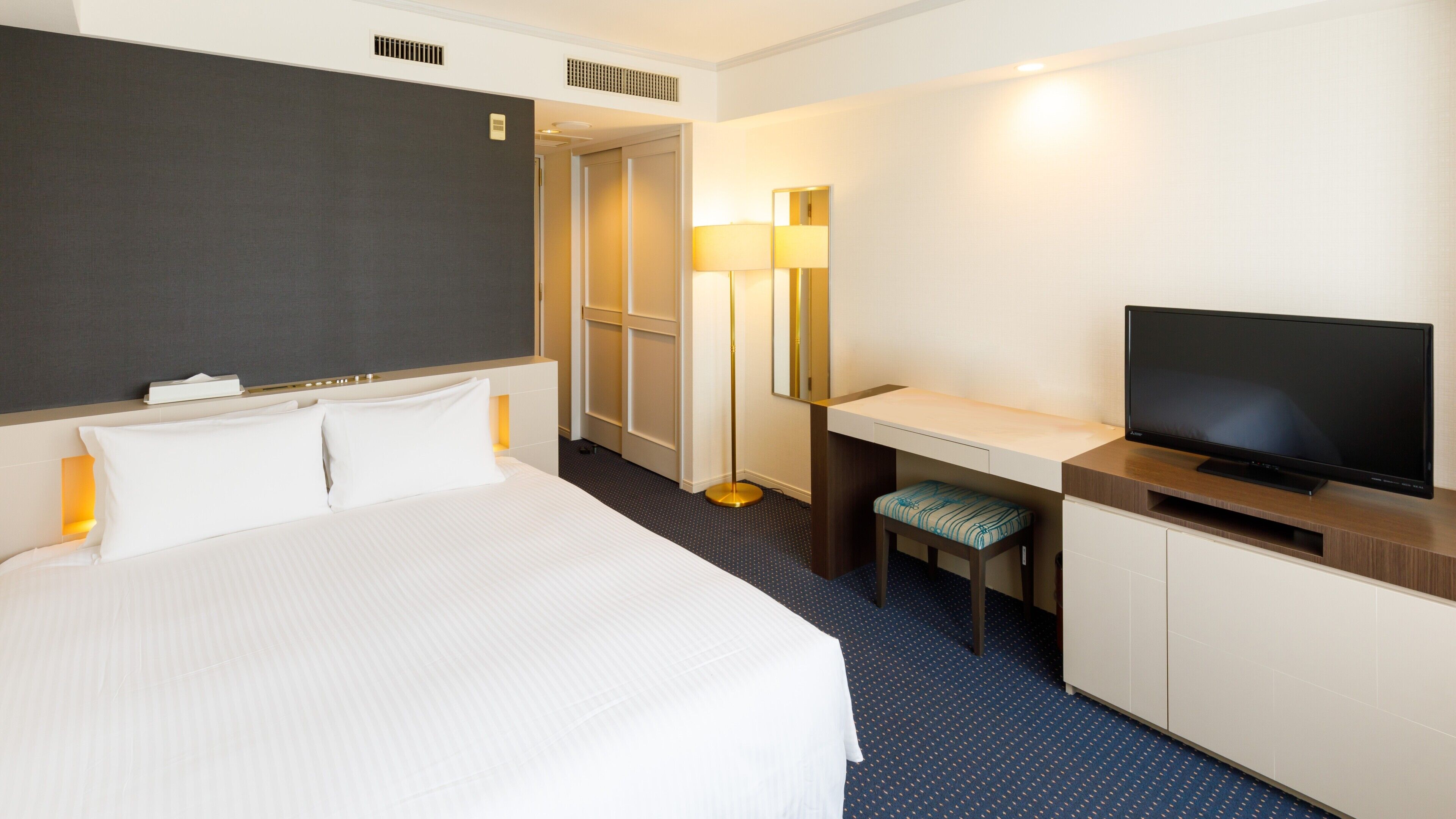 A hotel room with a bed, desk, chair, TV, and a mirror.