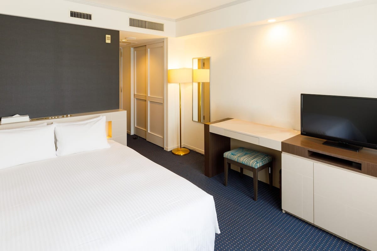 Hotellihuone, jossa on sänky, työpöytä, tuoli, televisio ja peili.