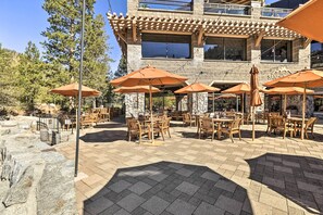 Une terrasse extérieure avec des tables en bois et des parasols orange, des murs en pierre et un grand bâtiment en arrière-plan.