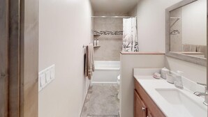 Un bagno stretto con una vasca, una doccia e un mobile lavabo con specchio.